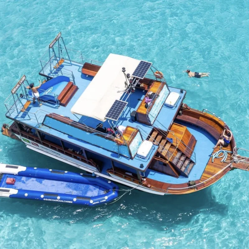 Barco de passeio visto de cima em água azul-turquesa, com pessoas nadando ao redor