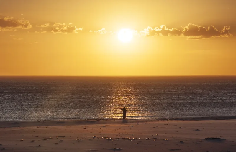 Sol sobre o mar de Arraial do Cabo com pessoa na areia