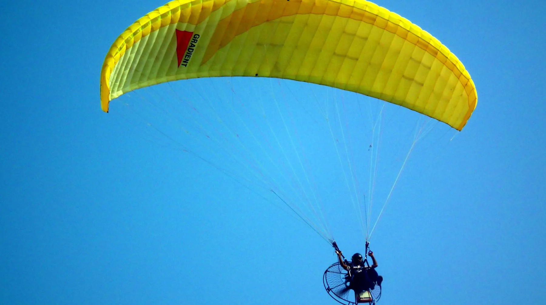 Paramotor com vela amarela sobrevoando o céu azul
